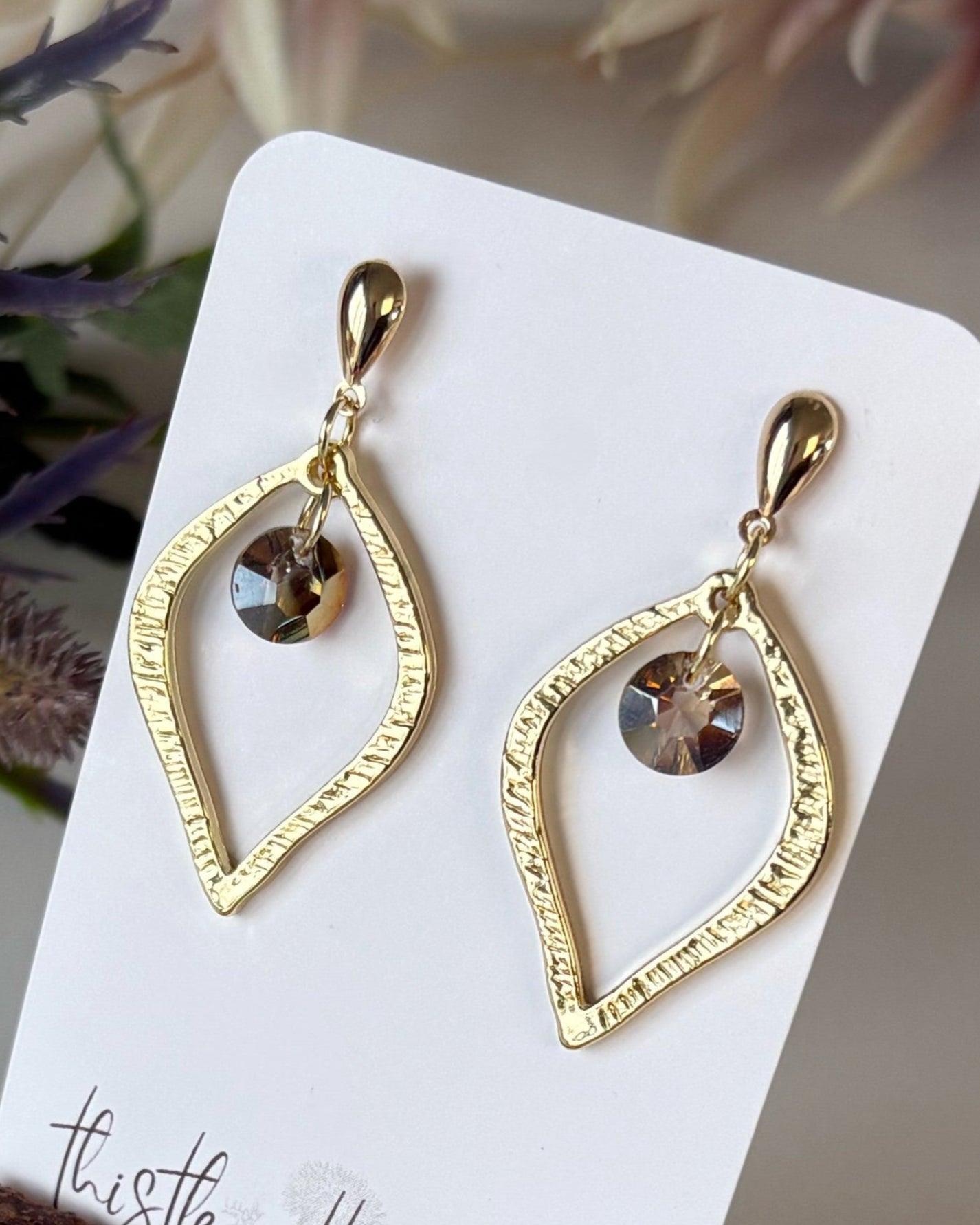 Gold earrings with heart-shaped design on a branded card with flowers in the background