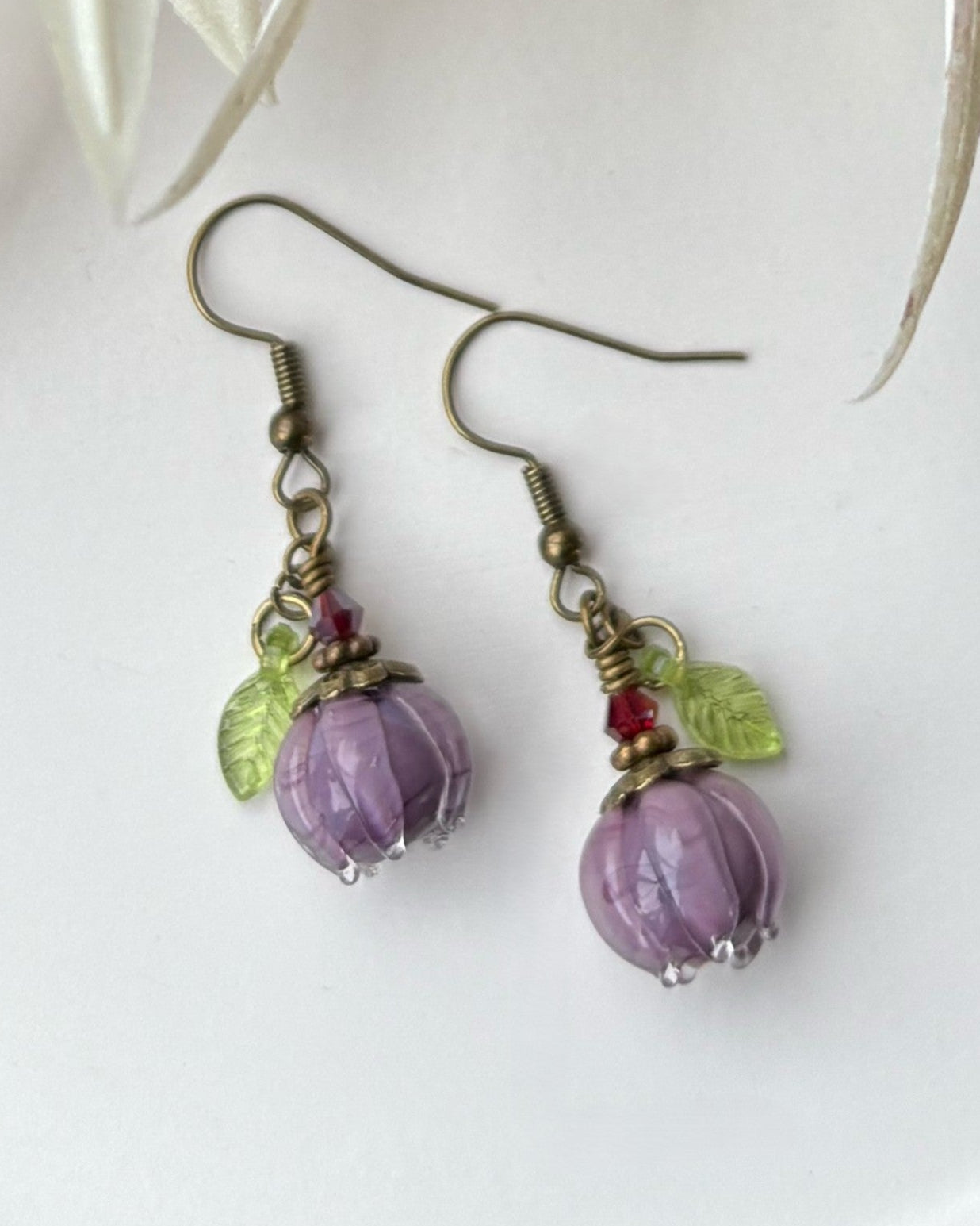 Pair of earrings with purple beads and green leaves on a white background