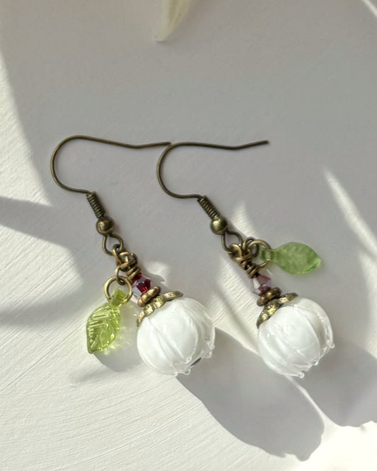 Pair of earrings with white beads and green leaves on a light background