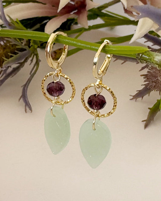 Gold earrings with green leaves and red stones on a floral background